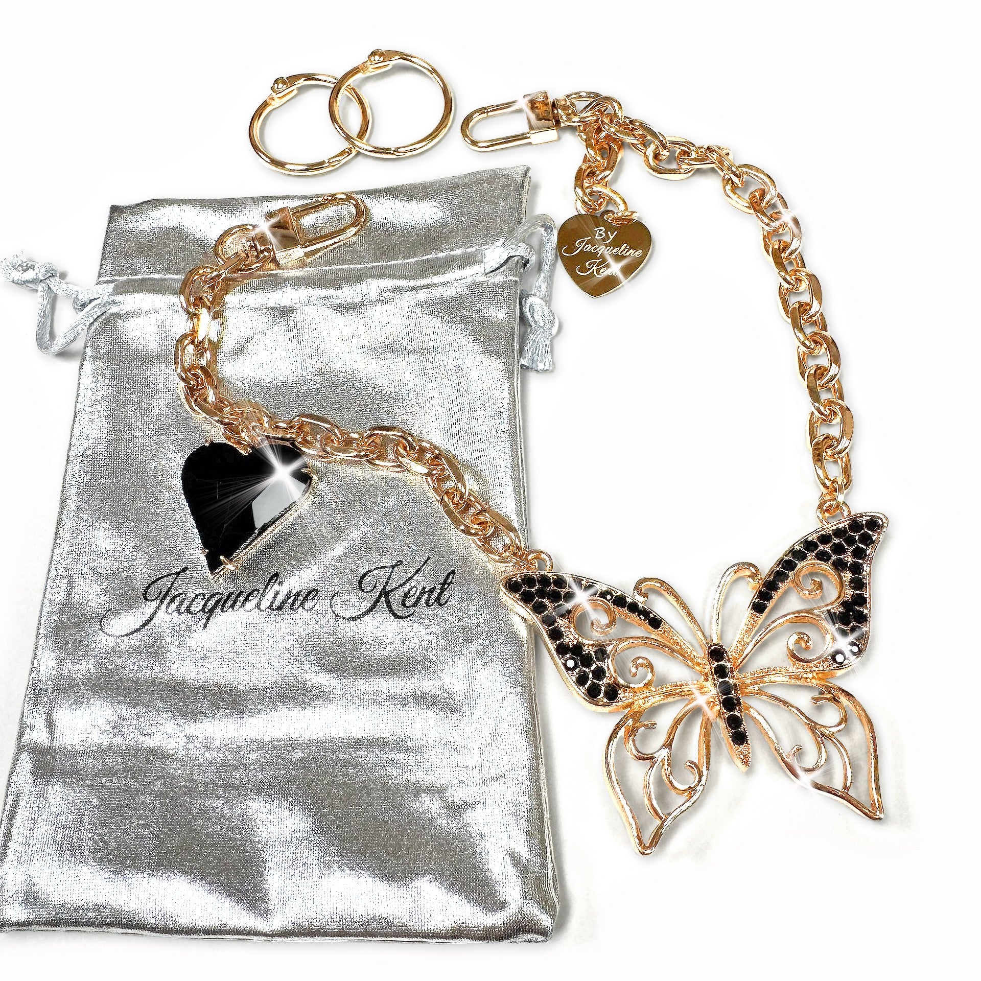 Gold charming chain with butterfly charm on a silver pouch, featuring the brand 'Jacqueline Kent'.