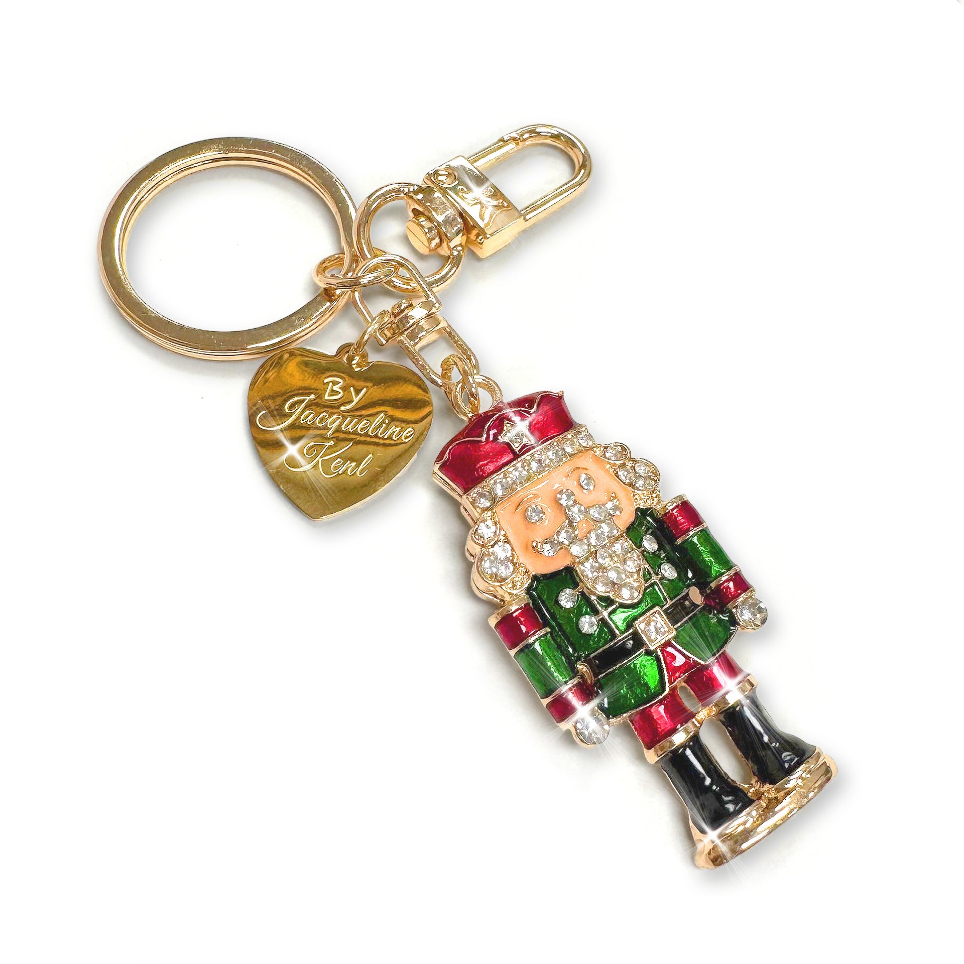 Gold nutcracker purse charm/keychain with black, green, red enamel and clear rhinestone details with heart shaped Jacqueline Kent branded tag on a white background