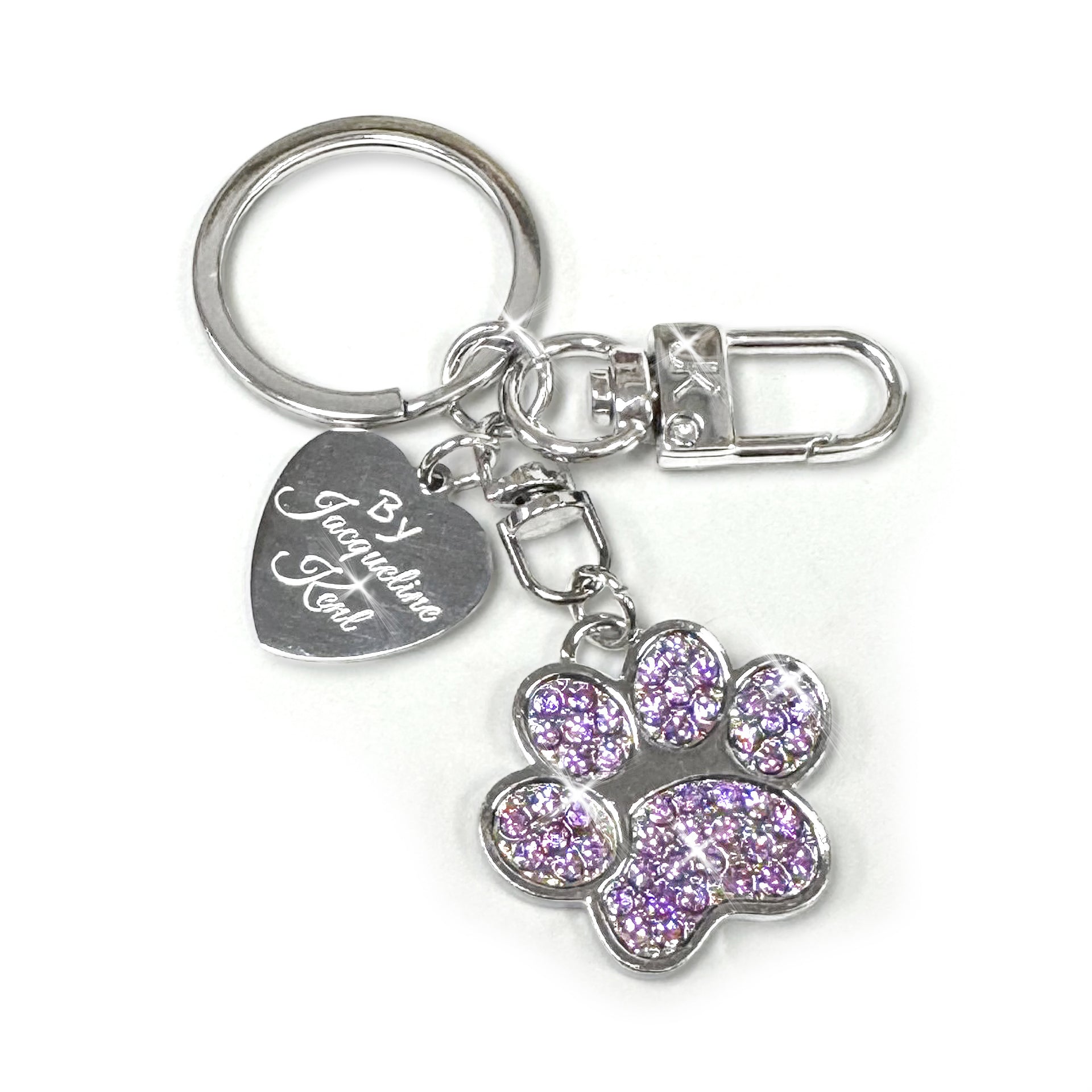 Silver purse/keychain with paw shaped charm encrusted in purple rhinestones with a heart shaped Jacqueiline Kent branded tag on a white background