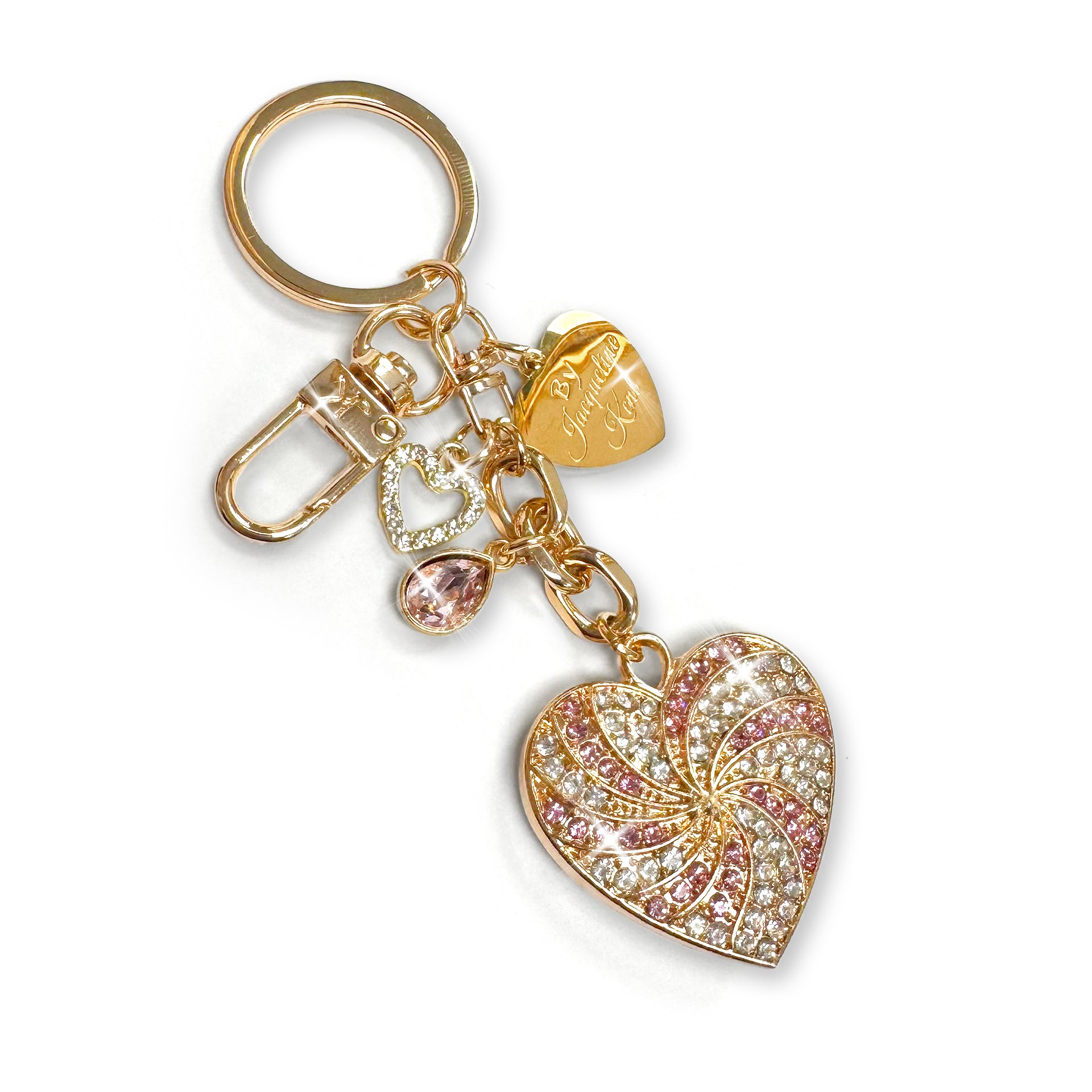 Clear and pink rhinestone encrusted gold heart-shaped purse charm/keychain in a spiral pattern with a Jacqueline Kent branded heart shaped tag and small crystal and heart shaped charms on a white background