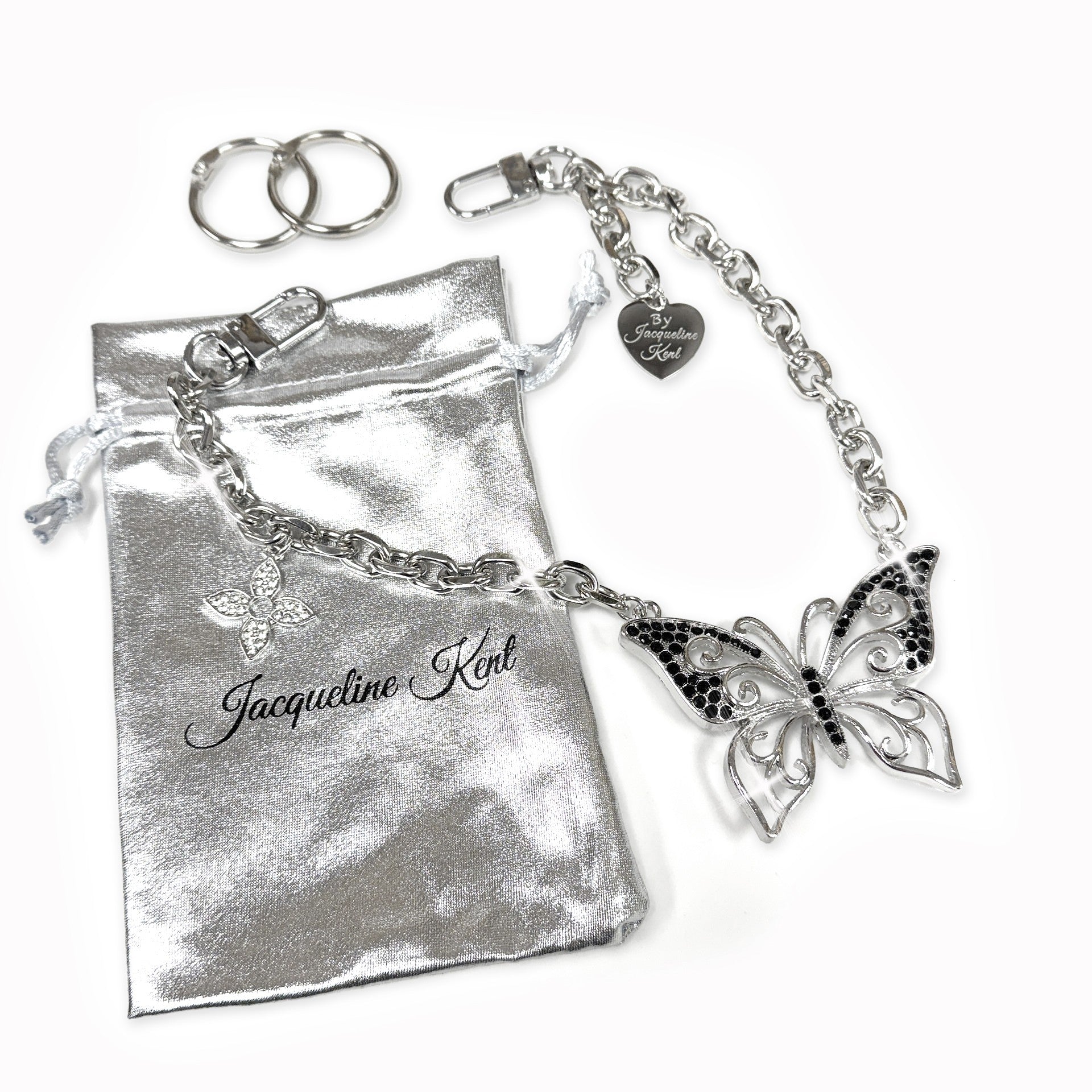 Silver butterfly charming purse chain and keychain on a silver pouch, branded 'Jacqueline Kent'.
