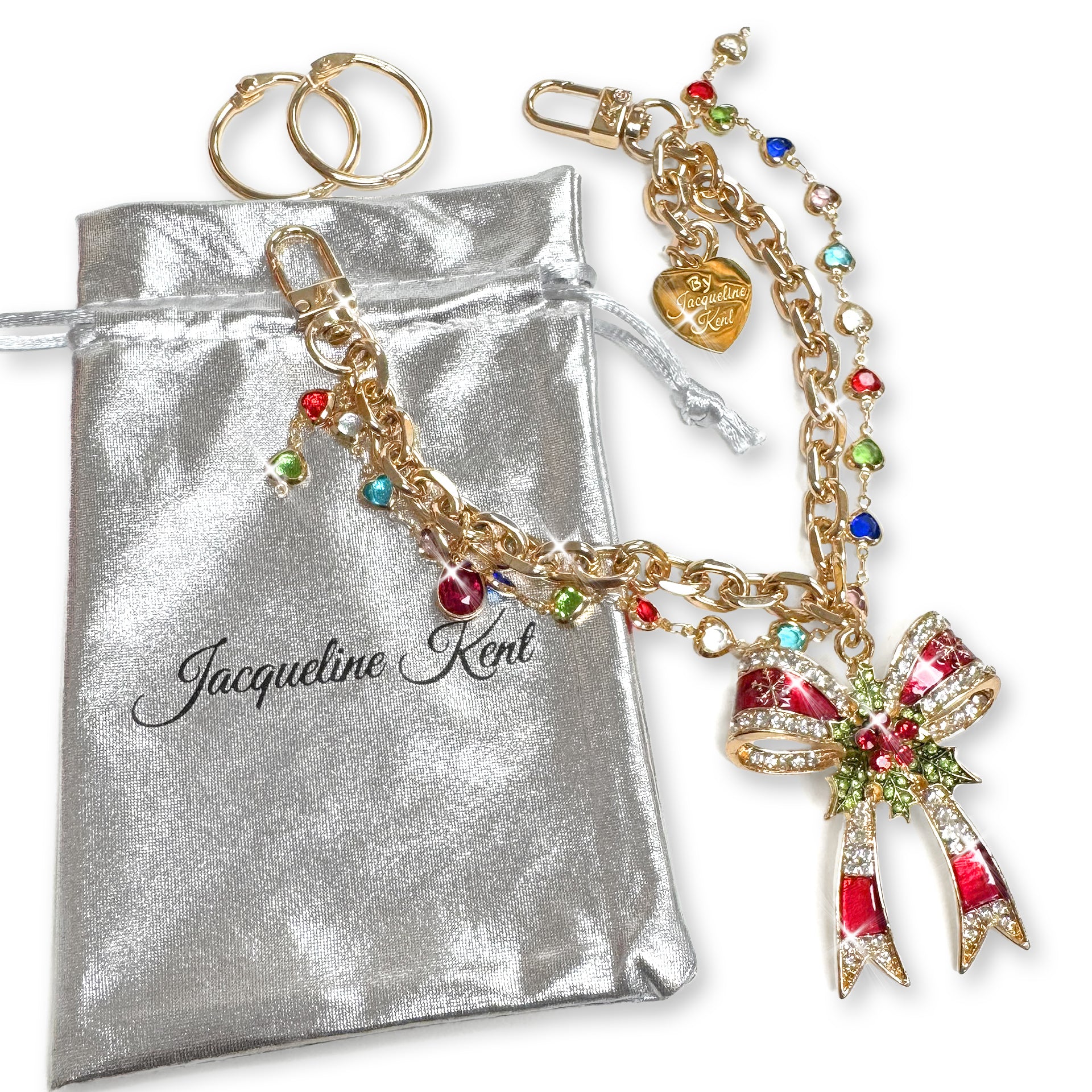 Gold purse charm with red enamelled bow encrusted with clear, red and green rhinestone details, and multi-coloured crystal charms with a Jacqueline Kent heart shaped branded tag on a while background