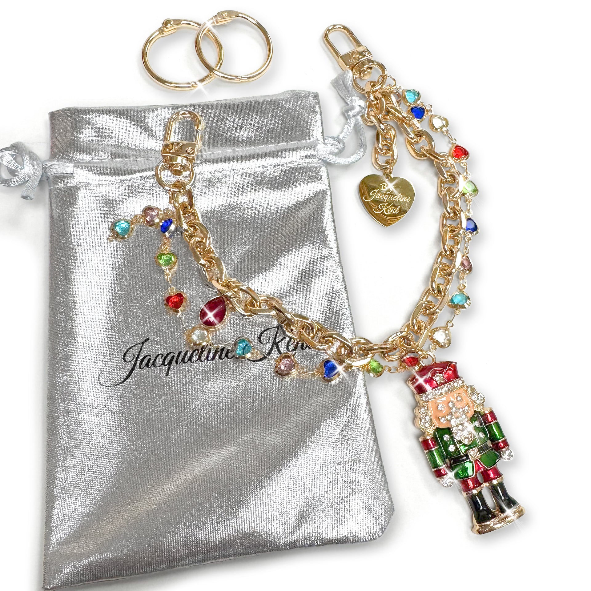 Gold purse charm with red and green enamelled nutcracker encrusted with clear, rhinestone details, and multi-coloured crystal charms with a Jacqueline Kent heart shaped branded tag on a while background